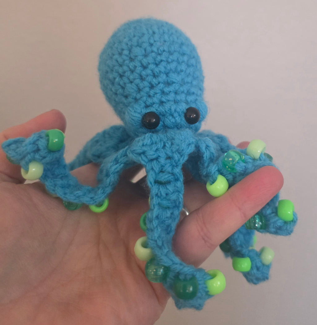 Blue knitted octopus toy held in a hand against a plain background