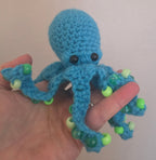 Blue knitted octopus toy held in a hand against a plain background
