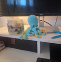 Crocheted blue octopus with beads on a desk next to a Dell monitor