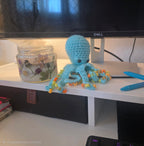Crocheted blue octopus with beads on a desk next to a Dell monitor
